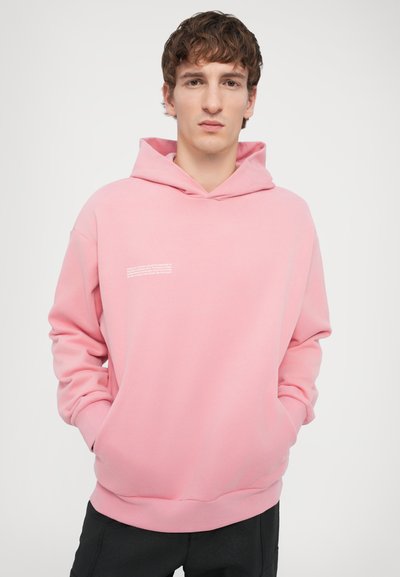 Hoodie en coton rose avec manches longues, poche kangourou, capuche avec cordon de serrage et texte blanc imprimé sur la poitrine. Texture lisse et coupe décontractée.