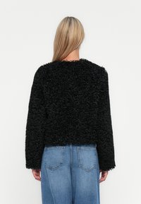 Μαύρο σακάκι από ψεύτικη γούνα με cropped σχέδιο, μακριά μανίκια και υφή. Συνδυασμένο με τζιν παντελόνι σε μπλε απόχρωση.