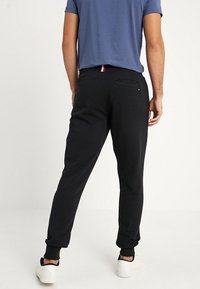 Czarne spodnie dresowe z prążkowanymi ściągaczami, z tylną kieszenią i paskiem w kolorze czerwono-biało-niebieskim na talii. Noszone z niebieską koszulką z krótkim rękawem.