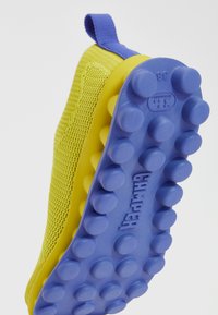 Κίτρινα sneakers από δίχτυ με μωβ καουτσούκ σόλα, διαθέτοντας υφή με μοτίβο για καλύτερη πρόσφυση. Διαθέτει θηλιά στο πίσω μέρος για εύκολη εφαρμογή.