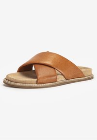 Sandale en cuir brun à enfiler avec des brides croisées, semelle intérieure en daim et semelle extérieure en caoutchouc cousue pour une bonne adhérence. Design plat avec un bout ouvert.