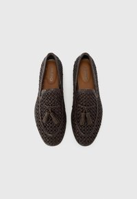 Braided brown leather slip-on shoes with a rounded toe, tassel accents, and a smooth inner lining. Minimalist design and textured surface.