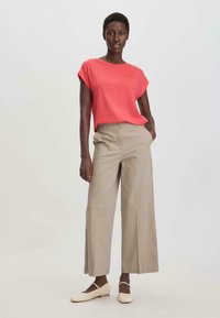 Koraalkleurig shirt met korte mouwen gecombineerd met beige wijde broek en lichtgekleurde flats. Glad textiel met een ontspannen pasvorm en zachte, lichte stof.