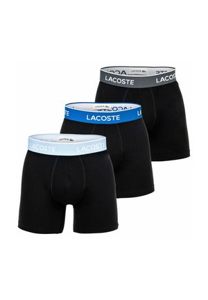 Drei schwarze Boxer-Slips mit elastischen Taillenbändern von Lacoste in Hellblau, Blau und Dunkelgrau, in einer versetzten Reihe angeordnet.