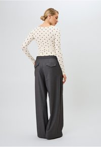 Ilga piedurkne tops ar melna riņķa rakstu uz krēmkrāsas fona, apvienots ar platām biksēm ar pelēku strecējumu, kas ir aprīkotas ar aizmugurējiem kabatām.