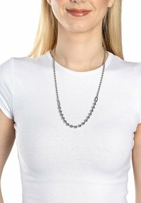Metalperlekæde med sfæriske sølvperler i forskellige størrelser, forbundet med glatte sølvforbindere, båret over en hvid t-shirt.