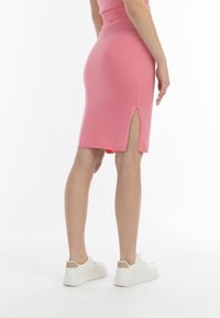 Fustă pencil tricotată roz, cu o fanta laterală, având un design ajustat și o textură netedă, asortată cu adidași albi.