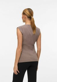 Top marron sans manches au design ajusté, texture lisse et coutures subtiles, associé à un pantalon noir. La vue arrière met en avant la silhouette galbée.