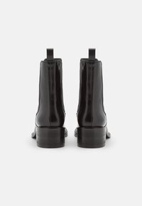 Botas de tobillo de cuero negro con un acabado brillante, paneles laterales elásticos y tiradores. Tacones de bloque negros y resistentes con una textura suave.