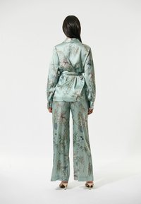 Lichtblauwe satijnen twee-delige set met bloemenpatroon, bestaande uit een blouse met pofmouwen en wijde broek. De stof heeft een glanzende afwerking.