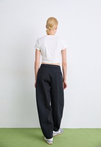 Pantalons noirs à jambes larges avec une texture lisse, dotés d'un détail de poche arrière. Associés à un t-shirt blanc ajusté cropped et des baskets grises.
