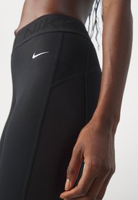 Närbild av en person som bär svarta Nike leggings med nätpaneler på sidorna, där Nike-logotypen syns på midjebandet och benet.