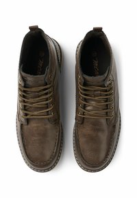 Botas de cuero marrón hasta el tobillo con ojetes metálicos, cordones dorados, costuras en contraste y acabado texturizado. Dos tiradores para facilitar el uso.