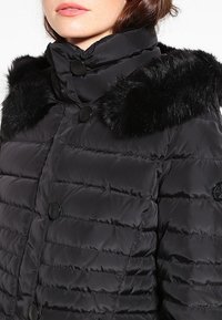 Černá péřová bunda s prošívaným designem, s límcem z umělé kožešiny a černými knoflíky. Materiál vypadá hladce a leskle.