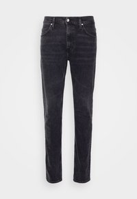 Černé džínové kalhoty vystavené vzpřímeně na bílém pozadí, s klasickým pětikapsovým střihem a zapínáním na knoflík.