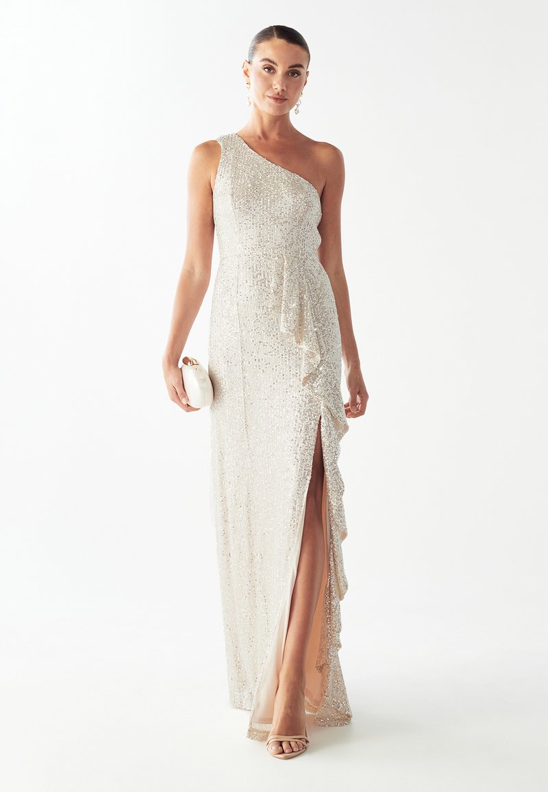 Vestido de noche de un solo hombro con lentejuelas en un tono beige claro, con detalles de volantes y una abertura en el muslo. Combinado con un bolso de mano blanco y tacones con tiras.