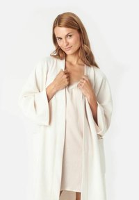 Weißer, knielanger Morgenmantel aus weichem Stoff mit weiten Ärmeln und einem schlichten Design. Das Innenkleidungsstück ist hellrosa mit Spitzenbesatz.