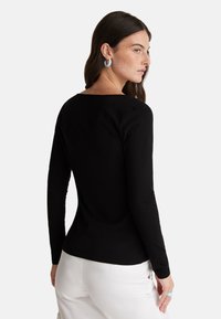Černý top s dlouhým rukávem a lodičkovým výstřihem, přiléhavý střih a hladká textura, kombinovaný s bílými kalhotami a modrými doplňky.