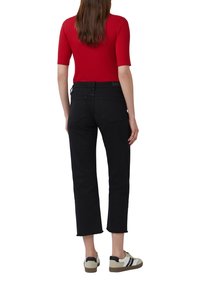 Jeans negros de pierna recta con dobladillo deshilachado, combinados con una blusa roja de manga corta y zapatillas beige con detalles en negro.