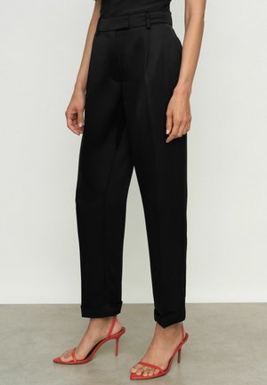 Mustade kohandatud püksid siledast kangast otse lõikega, mansetiga ja vöödega. Koos punaste kõrgete kontsadega sandaalidega.