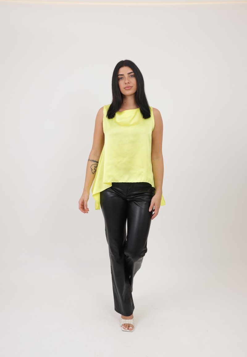 Top sin mangas de color amarillo claro con un dobladillo asimétrico y textura suave, combinado con pantalones ajustados de cuero negro. Fondo claro y neutro.