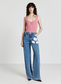 Body rosa senza maniche con un design arricciato, abbinato a jeans in denim blu a gamba larga con ricami floreali bianchi sulla tasca.