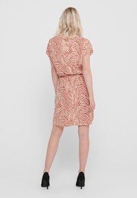 Vestido de manga corta, hasta la rodilla, en color durazno con un patrón de cebra, ceñido en la cintura, con un escote en V y tres detalles de corte.