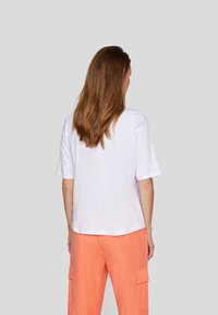 White cotton t-shirt with short sleeves, featuring a relaxed fit and round neckline, paired with orange cargo pants, showing back view.