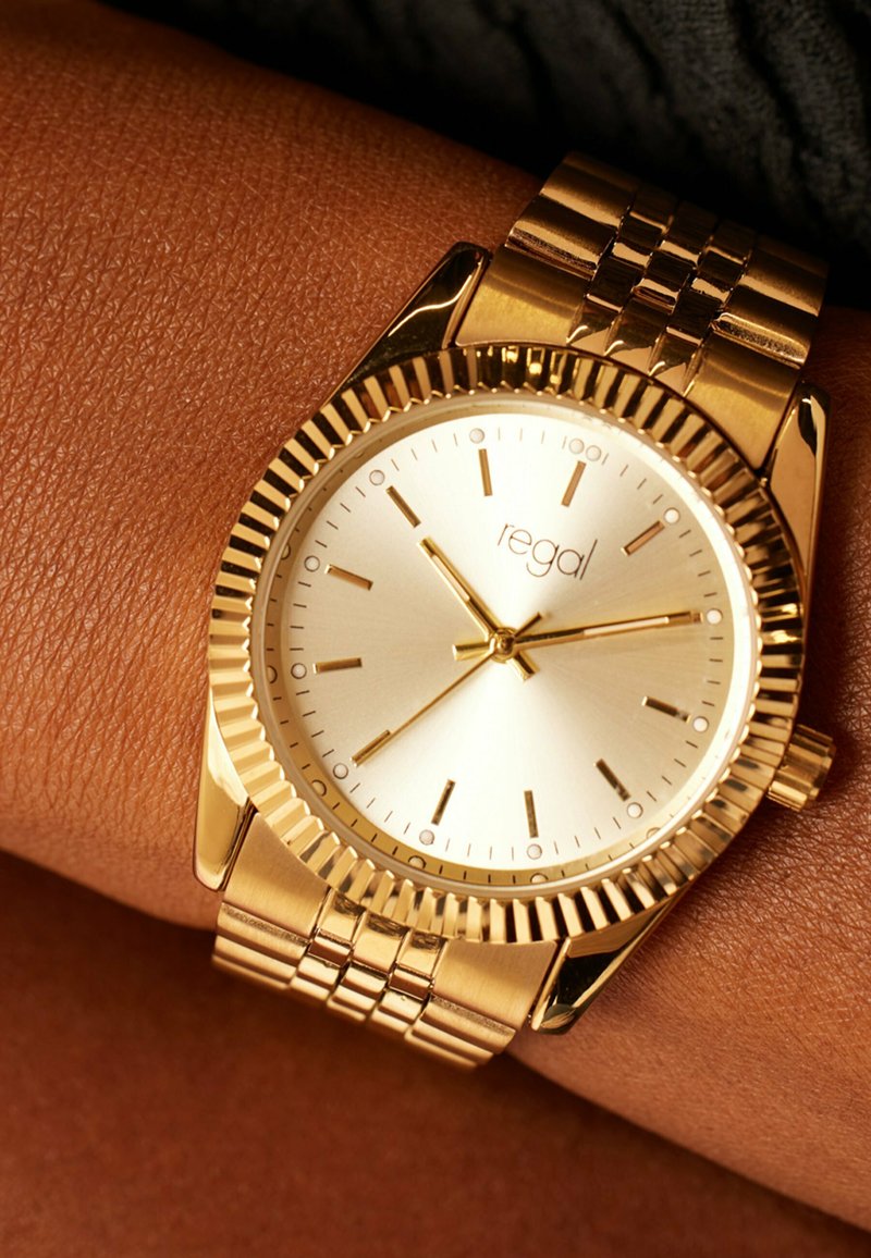 Gold-tone wristwatch with a metallic band, round case, and a reflective silver dial featuring hour markers and a textured bezel.