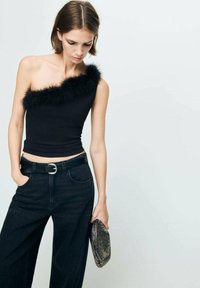 Sort top med én skulder og faux fur kanter, tætsiddende design. Kombineret med højtaljede mørke denimbukser og en clutch-taske med sølvdetaljer.