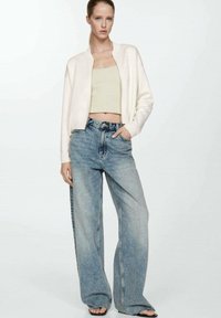 Light beige bomber jacket over a fitted mint green crop top, paired with wide-leg faded blue jeans and black sandals. Smooth fabric textures.