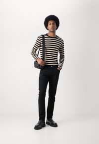 Stripete langermet skjorte i kremfarge og svart, paret med svarte slim-fit jeans og svarte sko, holder en liten svart crossover-veske.