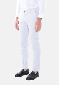 Pantaloni slim-fit grigio chiaro in cotone morbido, con fronte piatto, zip e tasche laterali discrete. Abbinati a mocassini in pelle nera.