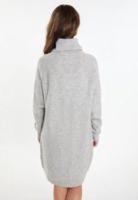 Graues Strickkleid mit hohem Kragen, langen Ärmeln und einer lockeren Form. Besitzt eine weiche Textur und einen leicht übergroßen Schnitt.
