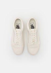 Beige Canvas-Sneaker mit strukturierter Oberfläche, weißen Schnürsenkeln, einem flachen Profil und einem grauen Streifen an den Seiten.