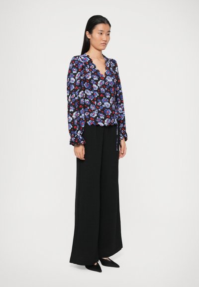 Blusa a maniche lunghe avvolgente floreale con scollatura a onde, caratterizzata da motivi blu, rossi e bianchi; abbinata a pantaloni neri a gamba larga.