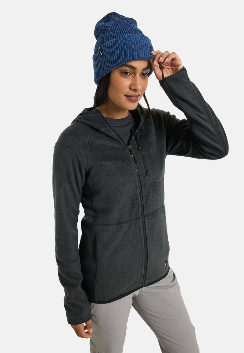 Black fleece jacket with a hood, zippered front, and two side pockets. Worn with a blue knitted beanie. Smooth texture, casual fit.