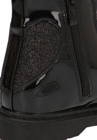 Bota de charol negra con un panel de tela texturizada negra, cremallera lateral y punta redonda; acabado suave con suela gruesa.