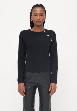 Zwart gebreid sweater met lange mouwen, ronde halslijn en decoratieve gouden knopen op de linkerschouder. Soepele textuur. Gecombineerd met zwarte broeken.