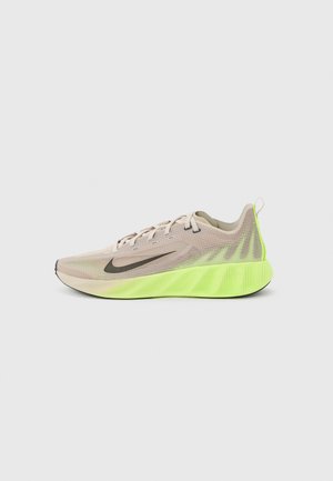 Lys beige løpesko med svart Nike-swoosh og lys neon grønn polstret såle på en ensfarget bakgrunn.
