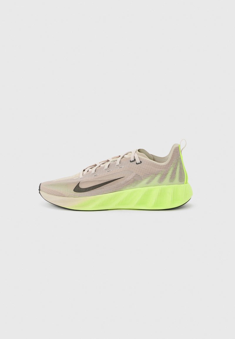 Chaussure de course beige clair avec le logo Nike noir et une semelle rembourrée vert néon vif sur un fond uni.