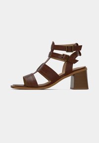 Καφέ δερμάτινα σανδάλια με ψηλό τακούνι, πολλαπλές λουρίδες, ρυθμιζόμενες αγκράφες και κρεμώδες μπλοκ τακούνι με υφή. Σχεδιασμός ανοιχτών δαχτύλων με λεία επιφάνεια.