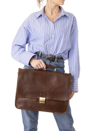 Brown leather briefcase with a front flap and gold hardware, held by a person wearing a blue and white striped shirt and denim.