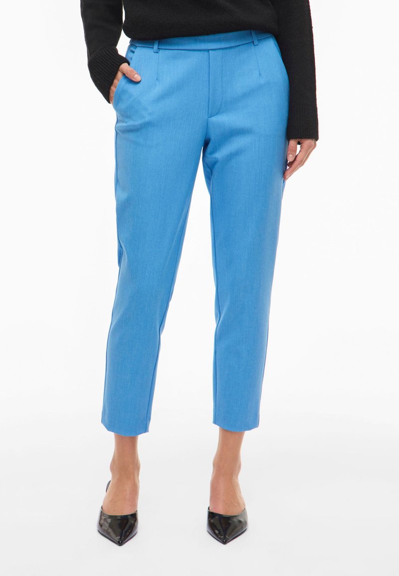 Sinised kohandatud püksid, millel on sile tekstuur, lühike pikkus, esiplikid ja küljetaskud, kombineeritud mustade teravate kandadega.