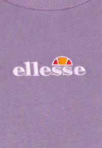 Logo ellesse blanc avec un demi-cercle orange et rouge au-dessus, brodé sur un tissu côtelé violet près d'un col rond.