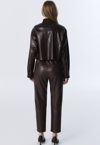 Bruine neplederen cropped jack met een geribbeld kraag, gecombineerd met bijpassende hooggetailleerde broek. Zachte textuur en een nauwsluitende pasvorm.