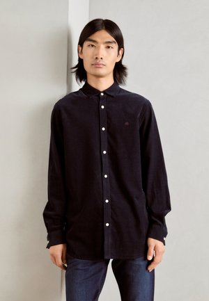 Navy button-up shirt made of soft fabric with a collar, featuring white buttons and a small embroidered detail on the chest. Worn with jeans.