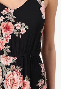 Svart blommig klänning med veckad textur, prydd med stora rosa och röda blommor, samt en slim fit midjedetalj.