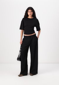 Sort cropped top med en tætsiddende talje, parret med brede sorte bukser. Footwear har leopardmønster. Modellen holder en lille sort taske.