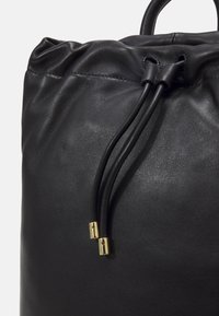 Černá kožená taška na stažení s hladkým povrchem, vyznačující se zlatými kovovými prvky a dvěma černými šňůrkami pro zavírání.